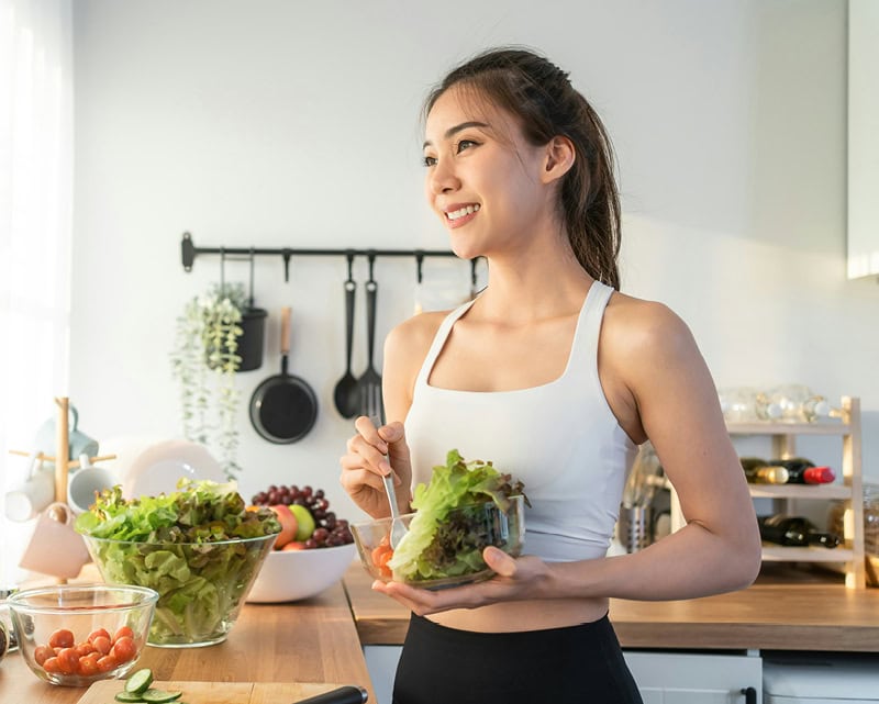 Smiling woman holding fresh salad bowl in modern kitchen