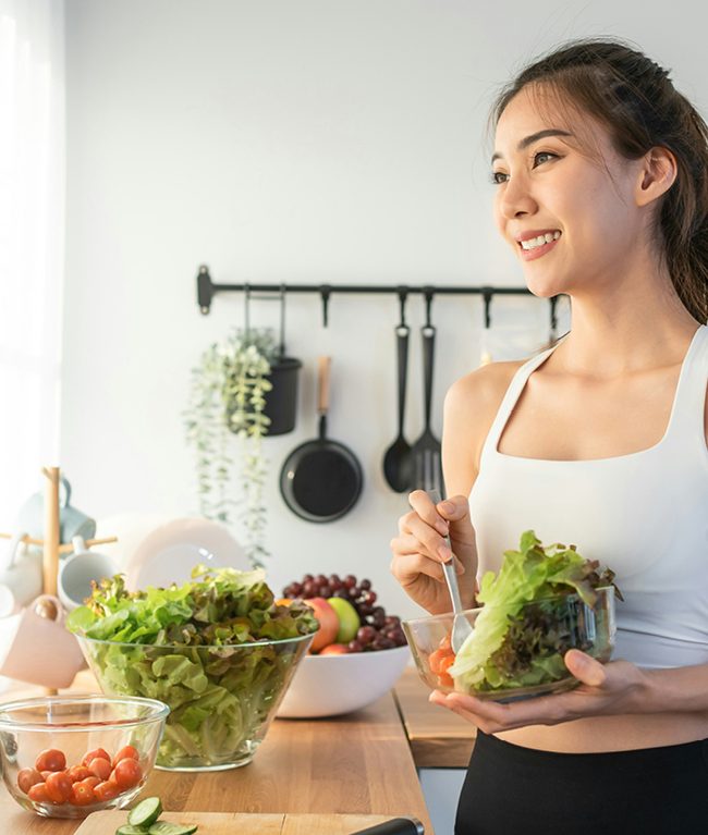Fit woman preparing salad in kitchen with fresh ingredients