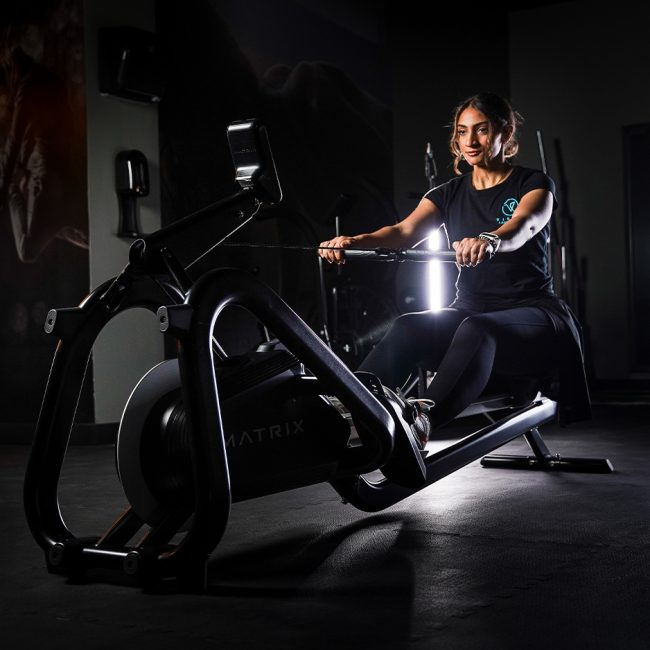 Woman doing indoor cycling in dark gym with neon lights
