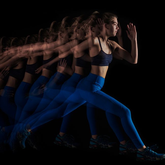 Woman running with blue motion blur in dark fitness studio