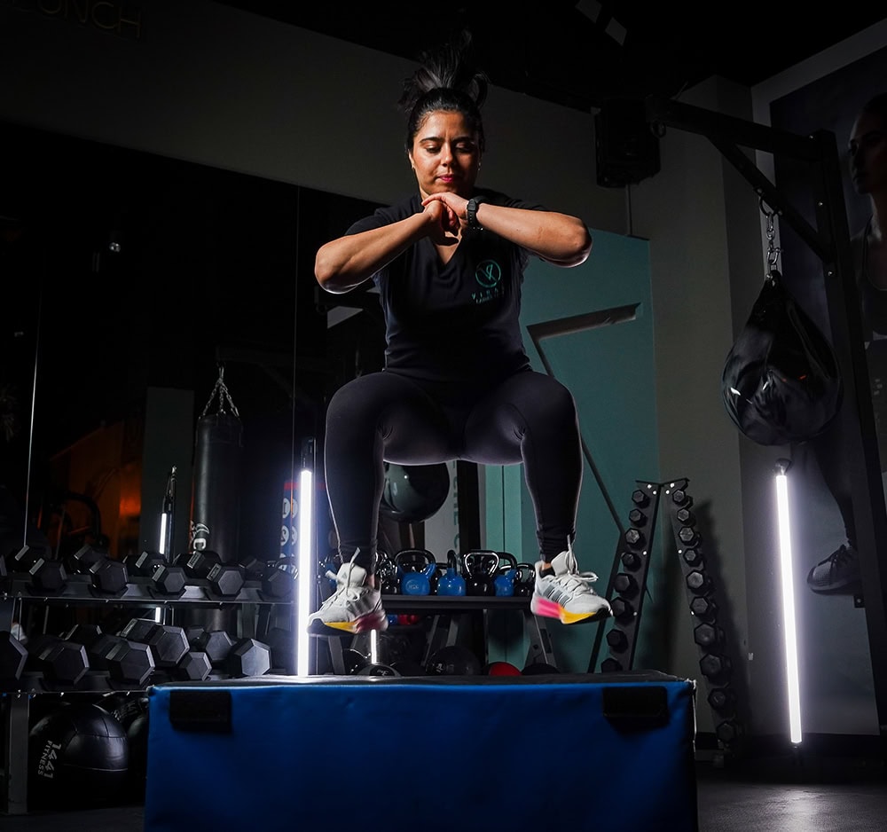 Woman performing explosive box jump exercise in a dark gym, showcasing strength and athleticism during functional training
