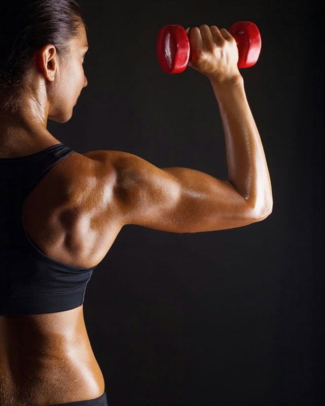 Close-up of toned arm lifting dumbbell in fitness studio