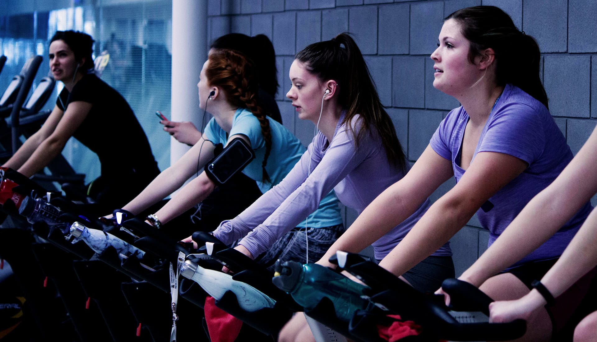Women riding spin bikes together in bright gym