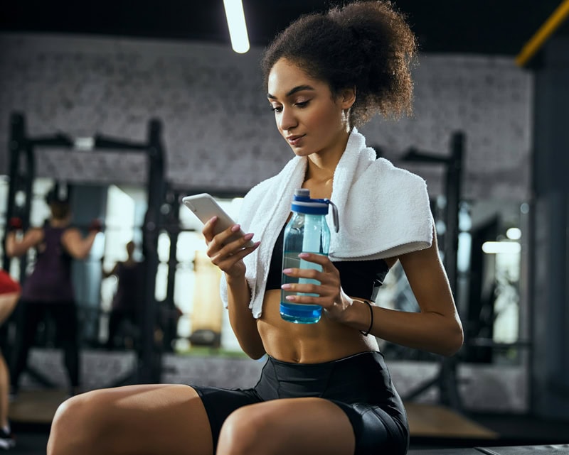 Woman in white towel sipping water after lifting session