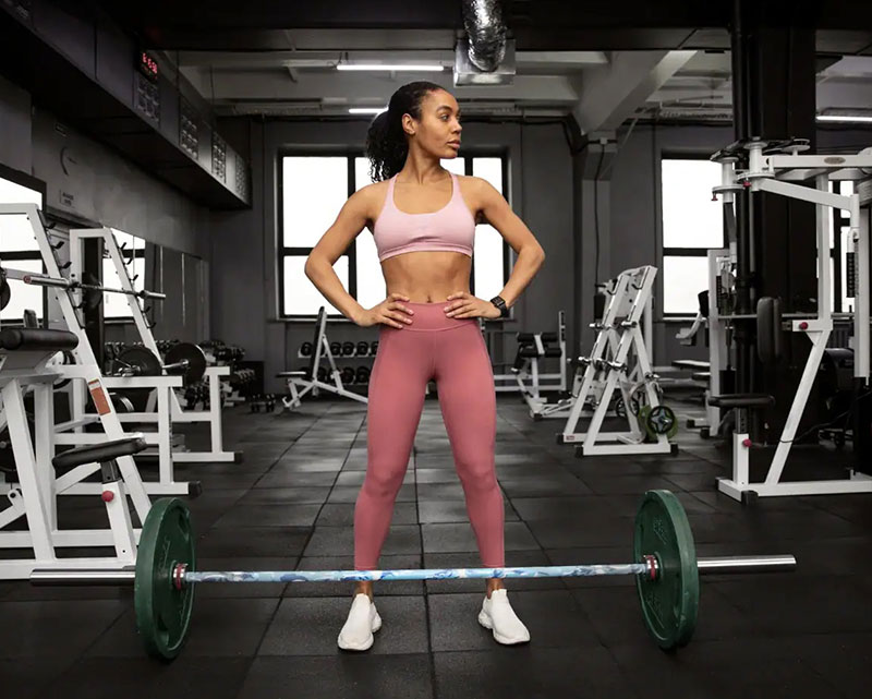 Female athlete posing with barbell in professional gym setup