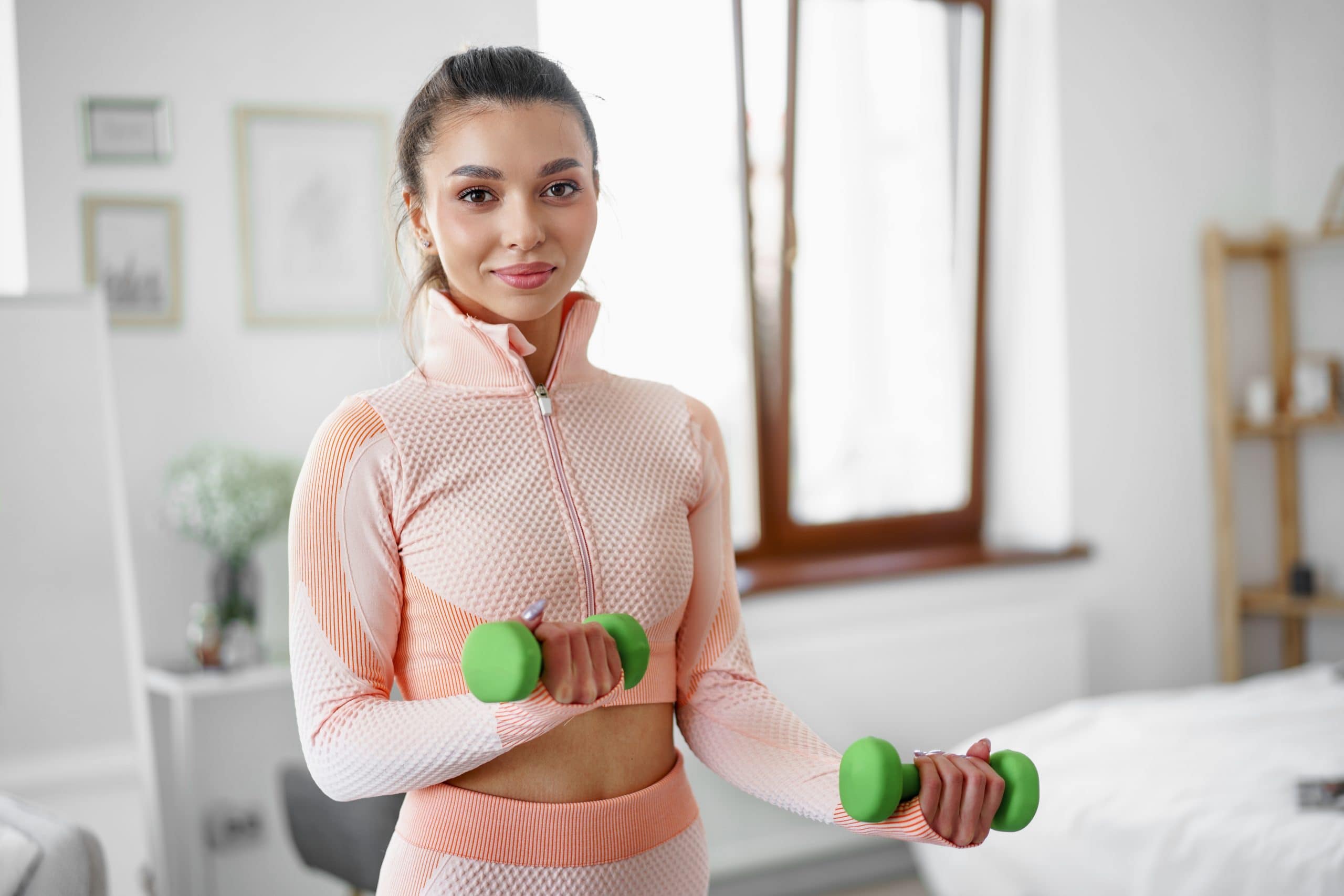 Sporty young woman exercising at home with dumbbells - women's health