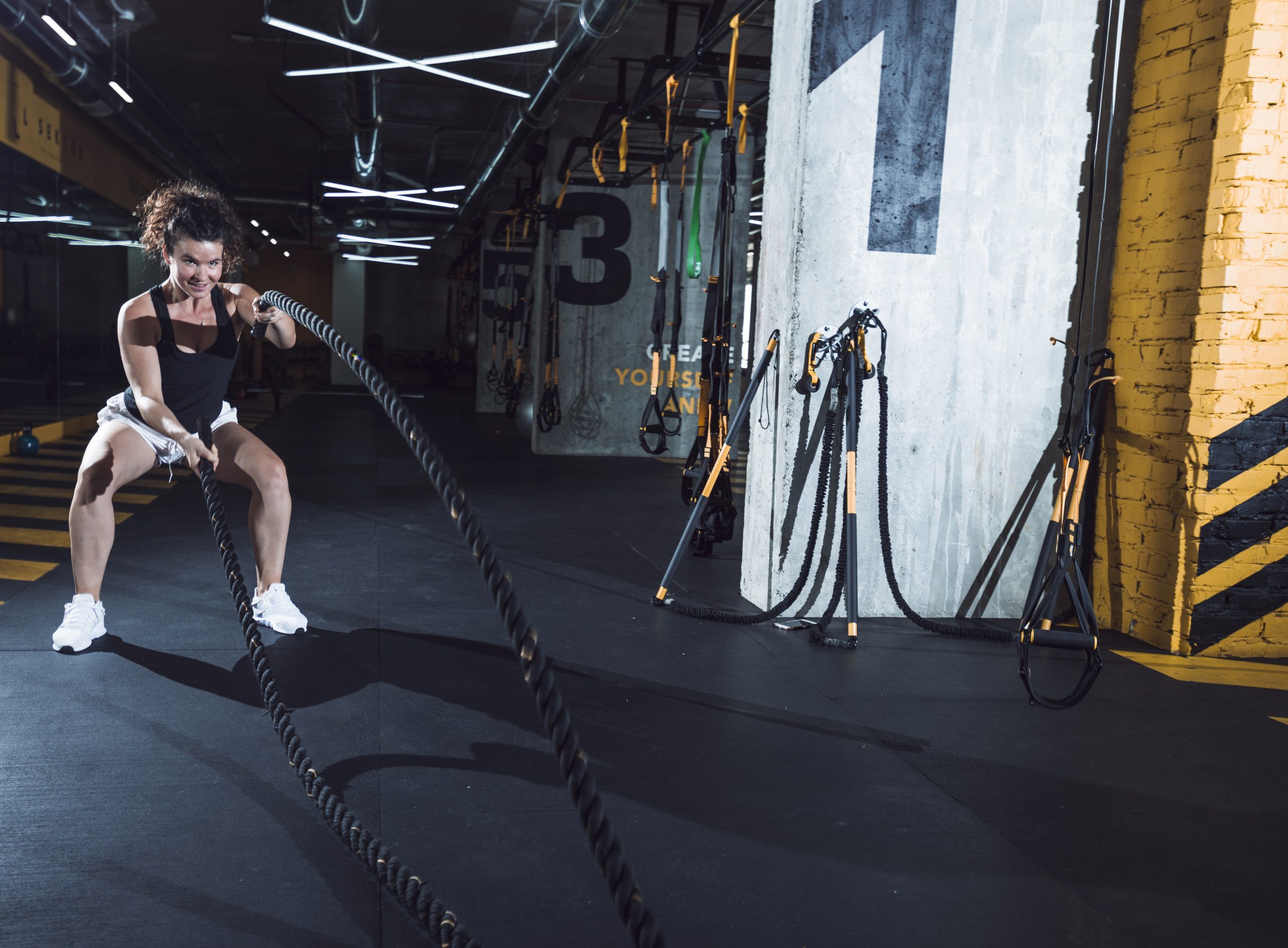 Smiling young woman exercising with battle ropes during a beginner-friendly CrossFit move
